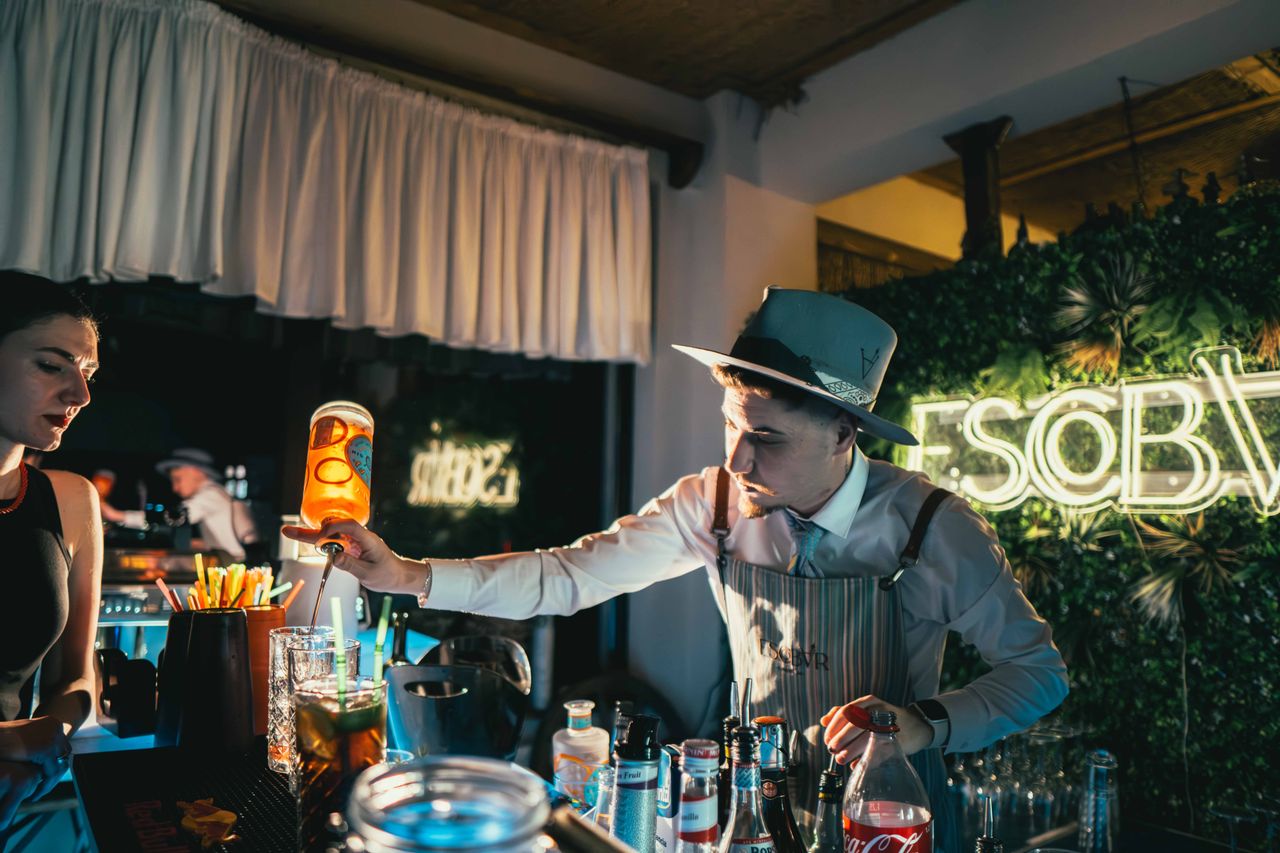 Bartender skillfully mixing a cocktail in a trendy neon-lit bar setting with lively ambiance.