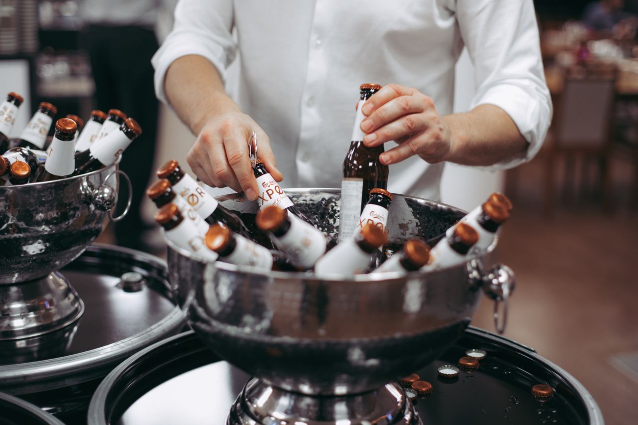 Close-up of a person placing beer bottles in ice buckets at an indoor event.