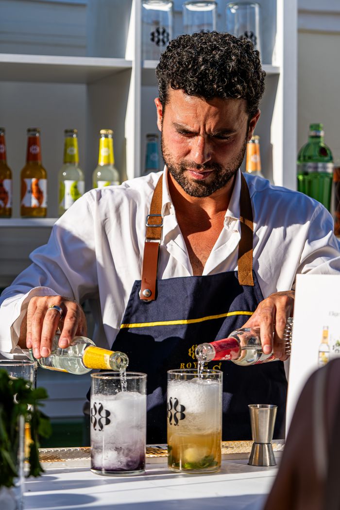 Bartender expertly crafting cocktails with bottles and garnishes at an outdoor bar, showcasing mixology skills.